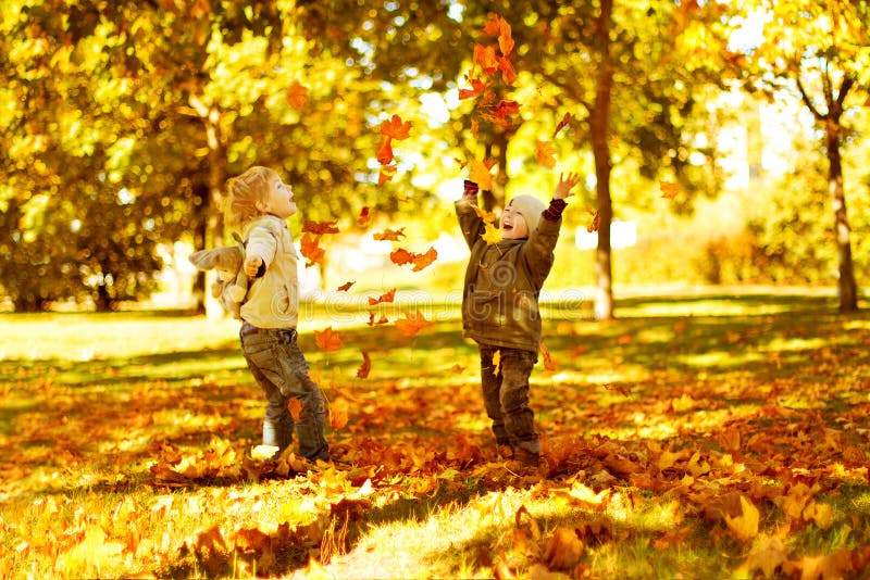 Children playing with autumn fallen leaves in park