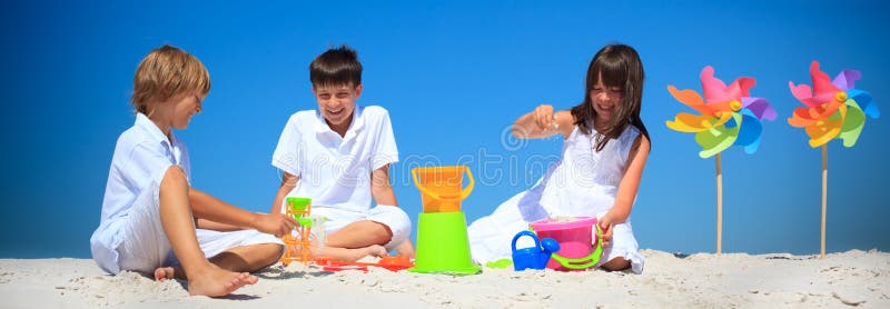 Panorama di tre bambini che giocano con i secchi di sabbia in una spiaggia.