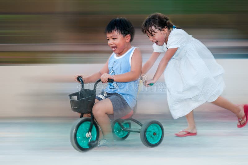 Young girl pushing tricycle with boy riding on it. Young girl pushing tricycle with boy riding on it.