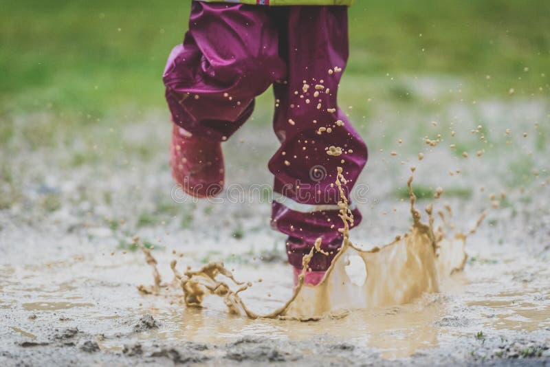 Children in rubber boots and rain clothes jumping puddle. Water is splashing from girls feet as she is jumping and playing in the rain. Protective rubber pants and jacket for playing in the mud. intentionally shot out of focus - blurred. Children in rubber boots and rain clothes jumping puddle. Water is splashing from girls feet as she is jumping and playing in the rain. Protective rubber pants and jacket for playing in the mud. intentionally shot out of focus - blurred