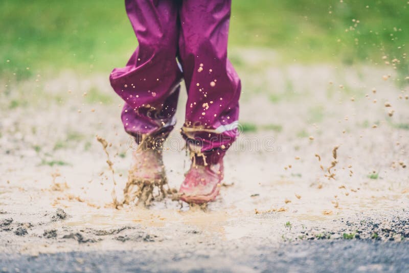 Children in rubber boots and rain clothes jumping puddle. Water is splashing from girls feet as she is jumping and playing in the rain. Protective rubber pants and jacket for playing in the mud. intentionally shot out of focus - blurred. Children in rubber boots and rain clothes jumping puddle. Water is splashing from girls feet as she is jumping and playing in the rain. Protective rubber pants and jacket for playing in the mud. intentionally shot out of focus - blurred