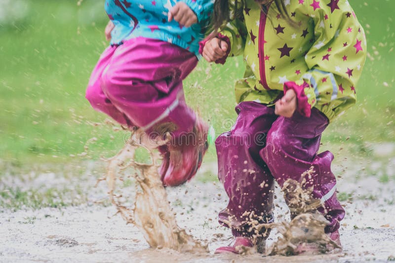 Children in rubber boots and rain clothes jumping in puddle. Water is splashing from girls feet as she is jumping and playing in the rain. Protective rubber pants and jacket for playing in the mud.