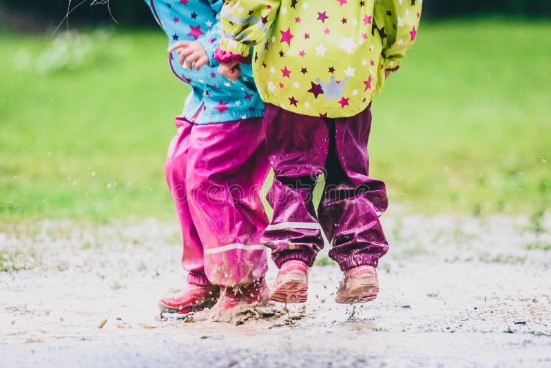 Children in rubber boots and rain clothes jumping in puddle. Water is splashing from girls feet as she is jumping and playing in the rain. Protective rubber pants and jacket for playing in the mud.