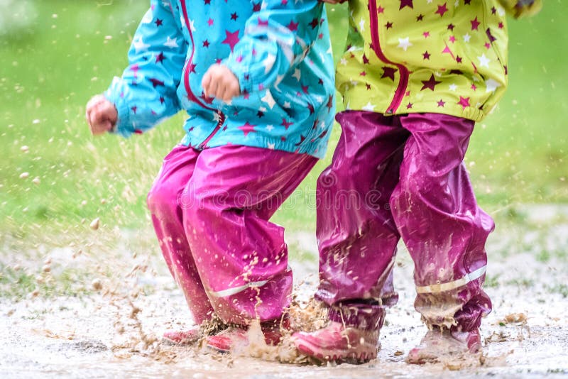 Children in rubber boots and rain clothes jumping in puddle. Water is splashing from girls feet as she is jumping and playing in the rain. Protective rubber pants and jacket for playing in the mud.