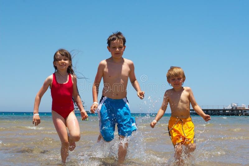 Three children running in shallow water at a beach. Three children running in shallow water at a beach.