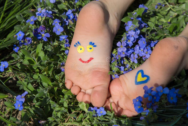 On children`s bare feet, lying among flowers, smiling face and a heart are drawn in yellow and blue