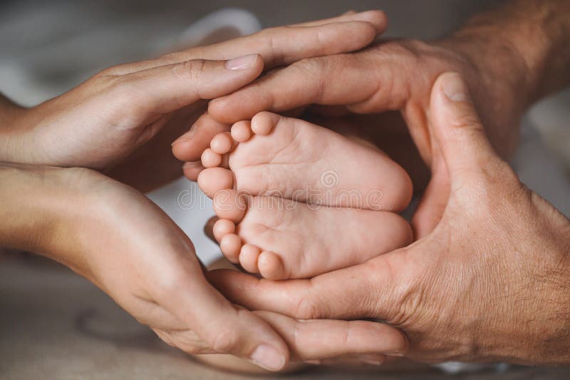 Tiny feet of a newborn baby caring father hugs with his big hands ,tender and gentle mother's hands,hug the arms of her husband and child,happy family,concept of love and care. Tiny feet of a newborn baby caring father hugs with his big hands ,tender and gentle mother's hands,hug the arms of her husband and child,happy family,concept of love and care