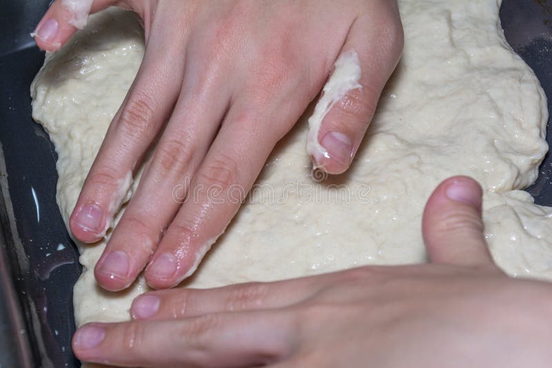 Children`s hands spread the pizza dough on a baking sheet. Cooking pizza at home. A popular Italian dish worldwide