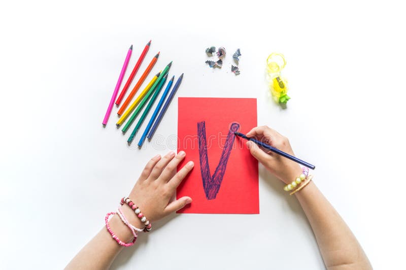 Children`s hands write the letter V colored pencils