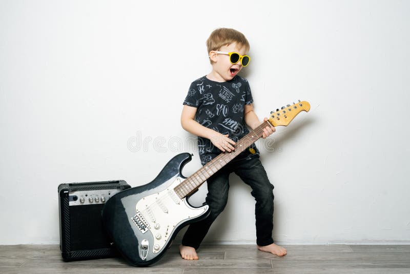 Children`s hobbies: a little boy in black glasses plays the electric guitar, imitates a rock star.