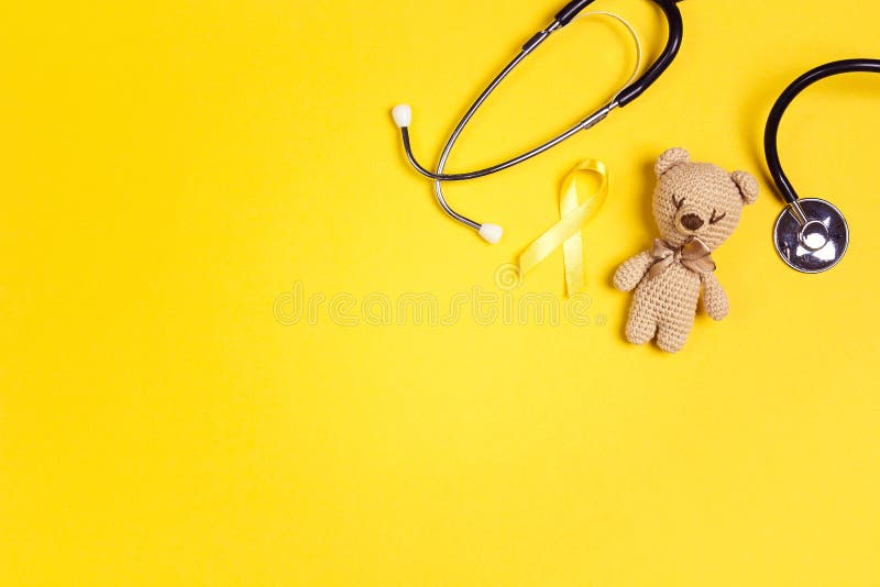 Children`s toy with a Childhood Cancer Awareness Yellow Ribbon and stethoscope on yellow background with copy space