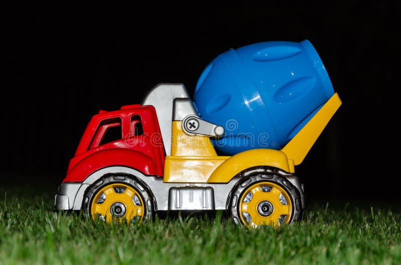 Children`s toy concrete mixer. Colored plastic baby car on grass background. Car Models. Kids toys. Closeup. At night royalty free stock image