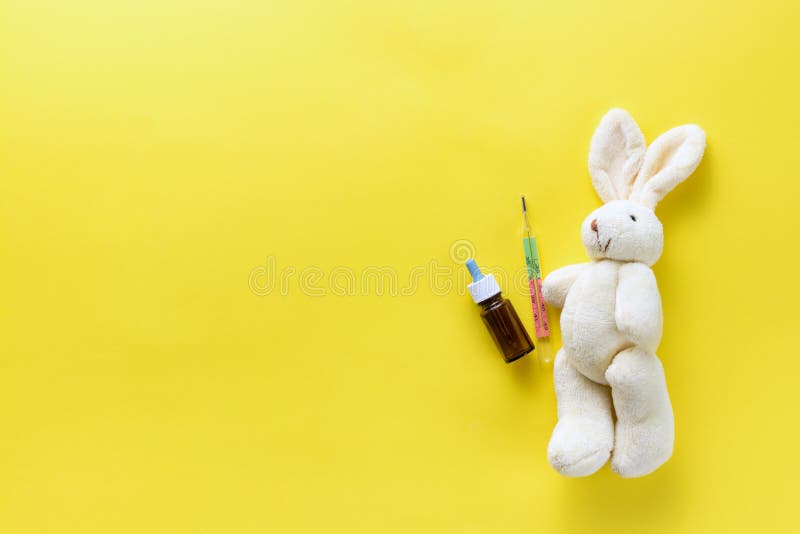 Children`s toy with a medical thermometer. Soft toy hare and medical thermometer on a yellow background. Chills in