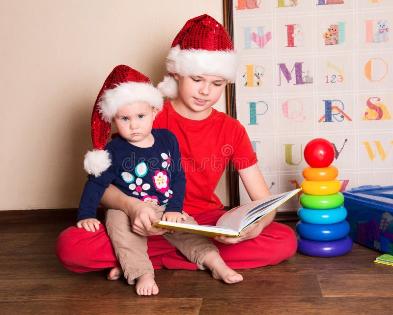 Children in Santa hats reading a Christmas book. Big brother reading to his little baby sister in the nursery. stock image Children in Santa hats reading a Christmas book. Big brother reading to his little baby sister in the nursery. stock image