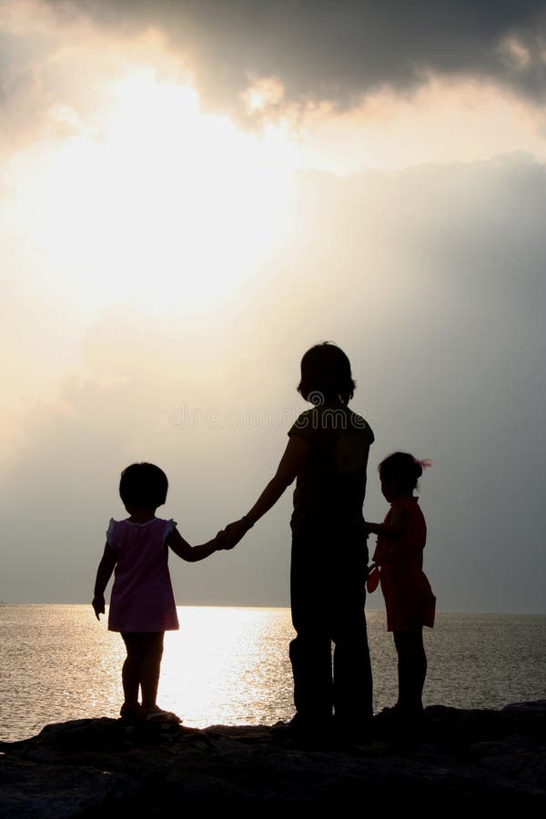 Three children stand silhouetted against the sunset on a beach overlooking the ocean. Three children stand silhouetted against the sunset on a beach overlooking the ocean.