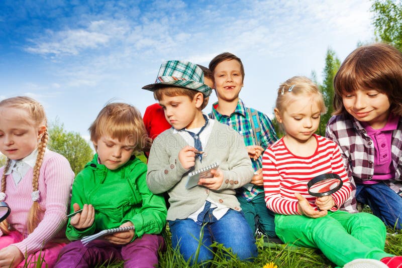 Children sitting with magnifier and writing notes stock photography