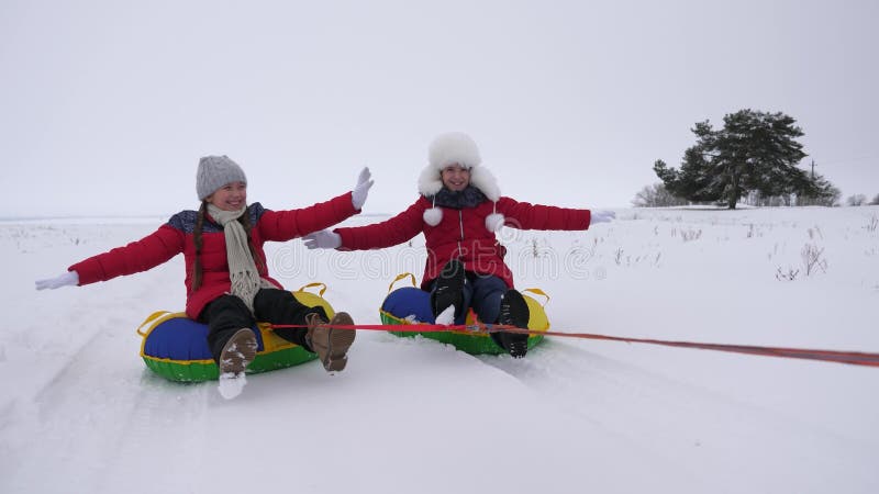 Children slides in snow on an inflatable snow tube and waves hand. Happy girls slides through snow on sled. kids playing