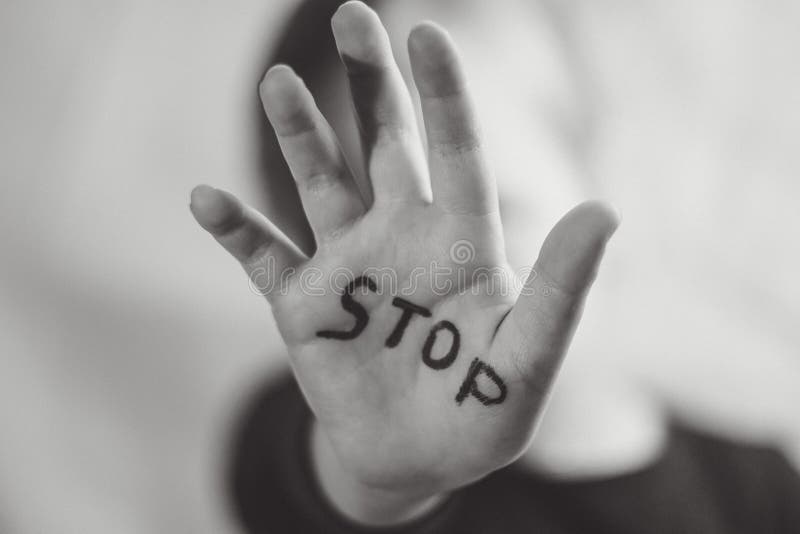 Little frightened girl shows the word `Stop` written on the arm. Children are subjected to violence and publishing in the home and