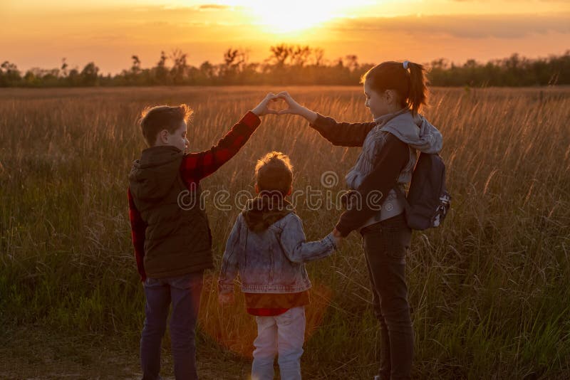 Children at sunset in the field show a heart from their fingers. Walk in the fresh air. Silhouette of three children. Beautiful sunset. A happy family