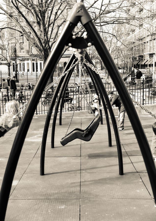 Swinging on a swing set in a city park in black and white or sepia tone children playing and laughter. Swinging on a swing set in a city park in black and white or sepia tone children playing and laughter