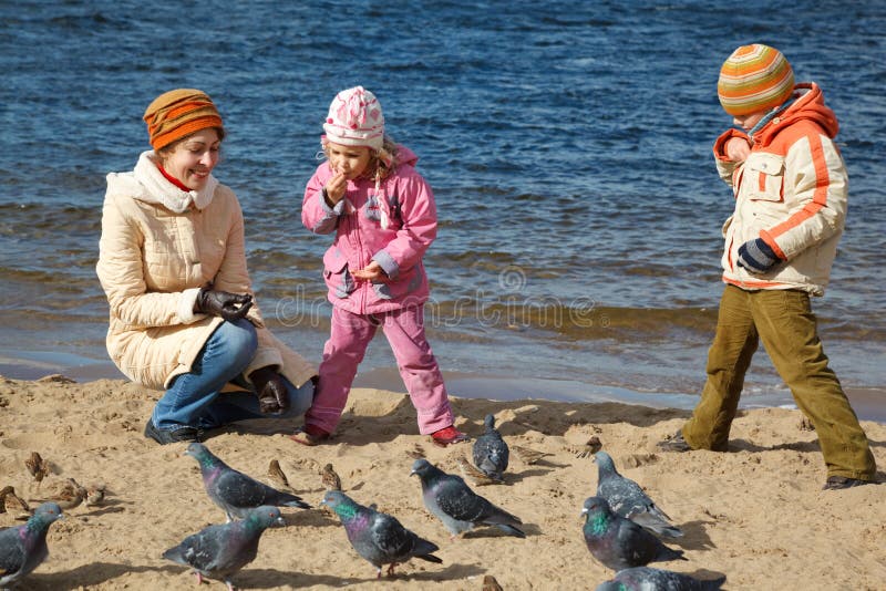 Children together with mum feed birds on autumn