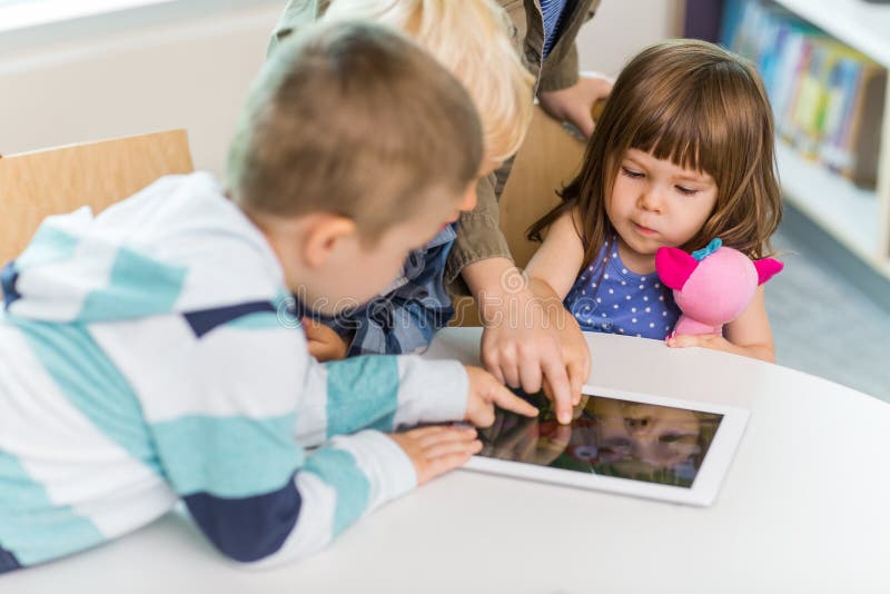 Cute girl with friends using digital tablet at table in school library. Cute girl with friends using digital tablet at table in school library