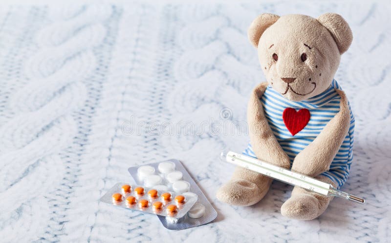 Children s soft toy teddy bear with pills takes the temperature of a mercury glass thermometer. child  disease.