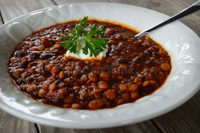 A white bowl of quinoa lentil chili topped with sour cream and parsley. A white bowl of quinoa lentil chili topped with sour cream and parsley.