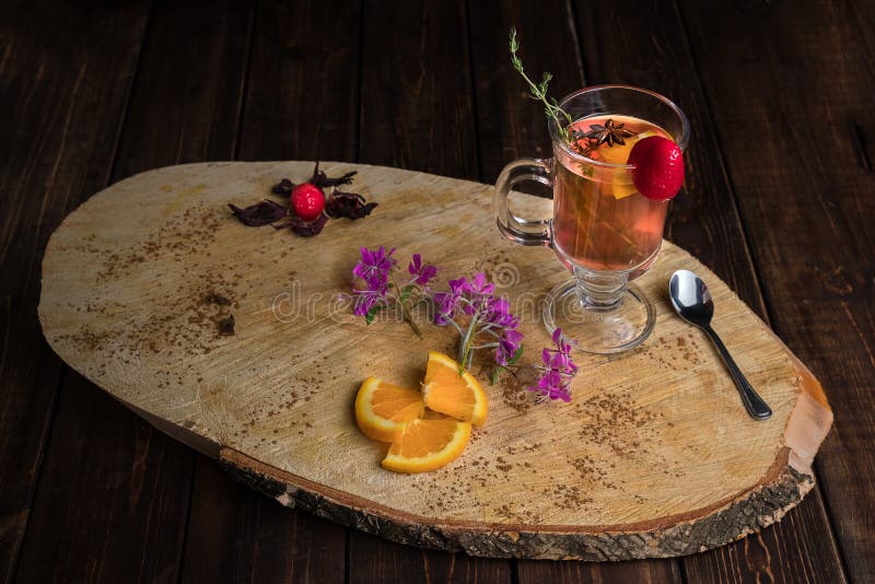 Chili cinnamon bourbon hot toddy in transparent glass on wooden cross section of trunk tree decorated with mint, strawberry and orange. Chili cinnamon bourbon hot toddy in transparent glass on wooden cross section of trunk tree decorated with mint, strawberry and orange