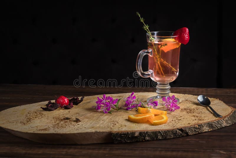 Chili cinnamon bourbon hot toddy in transparent glass on wooden cross section of trunk tree decorated with mint, strawberry and orange. Copy space for menu. Chili cinnamon bourbon hot toddy in transparent glass on wooden cross section of trunk tree decorated with mint, strawberry and orange. Copy space for menu