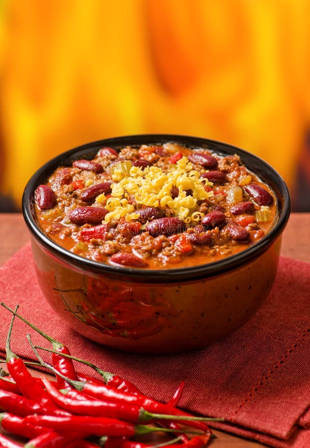 A spicy bowl of chili con carne with peppers against a fire background.