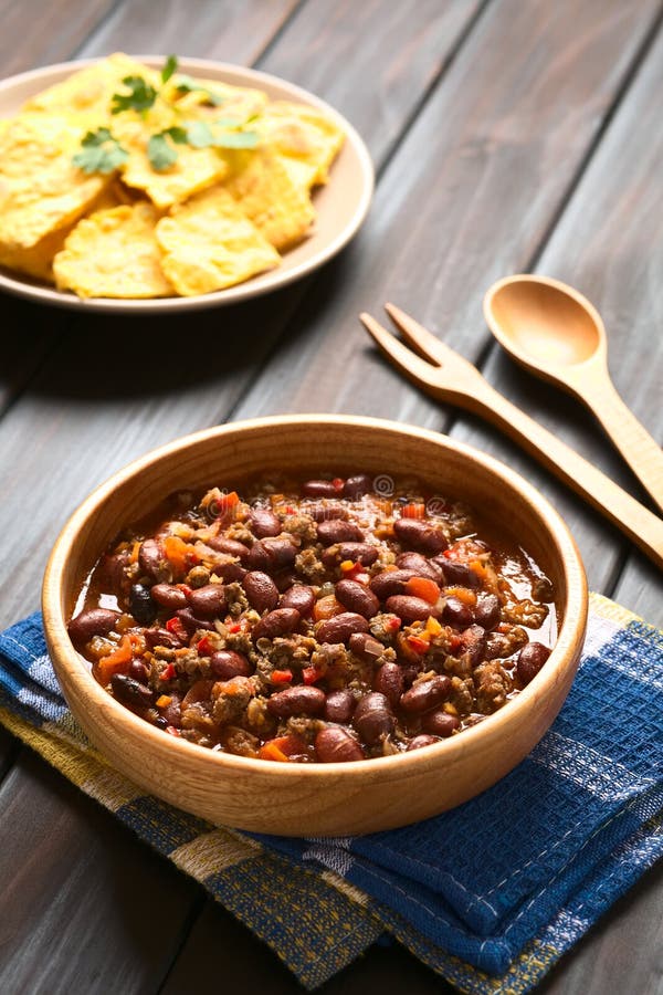 Chili con carne with homemade tortilla chips in the back, photographed with natural light (Selective Focus, Focus in the middle of the chili)