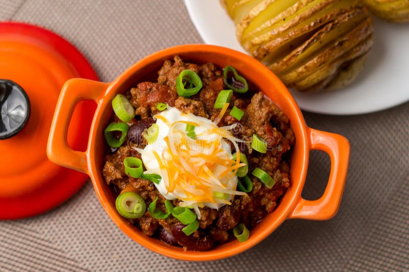 Fresh homemade bowl of chili con carne with beans, sour cream, grated cheddar cheese and green onions. Served with hasselback potatoes on the side. Fresh homemade bowl of chili con carne with beans, sour cream, grated cheddar cheese and green onions. Served with hasselback potatoes on the side.