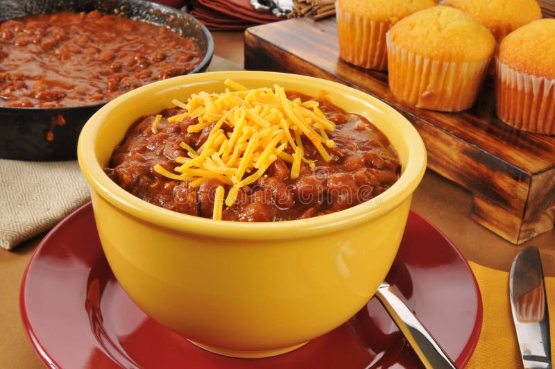 A bowl of chili con carne with cheddar cheese and cornbread muffins. A bowl of chili con carne with cheddar cheese and cornbread muffins