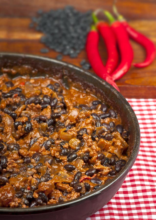 Hot and spicy Chili con Carne in the frying pan with rice. Whole red peppers and raw black beans in the background. Hot and spicy Chili con Carne in the frying pan with rice. Whole red peppers and raw black beans in the background.