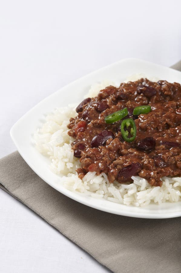 A tabletop view of a plate of chili con carne on white rice, garnished with green chili peppers. A tabletop view of a plate of chili con carne on white rice, garnished with green chili peppers.