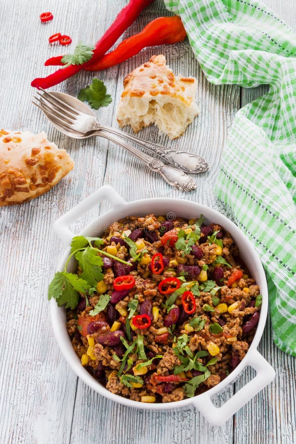 Chili con carne in a white casserole on wooden table with fresh vegetables and bread. royalty free stock photos Chili con carne in a white casserole on wooden table with fresh vegetables and bread. royalty free stock photos