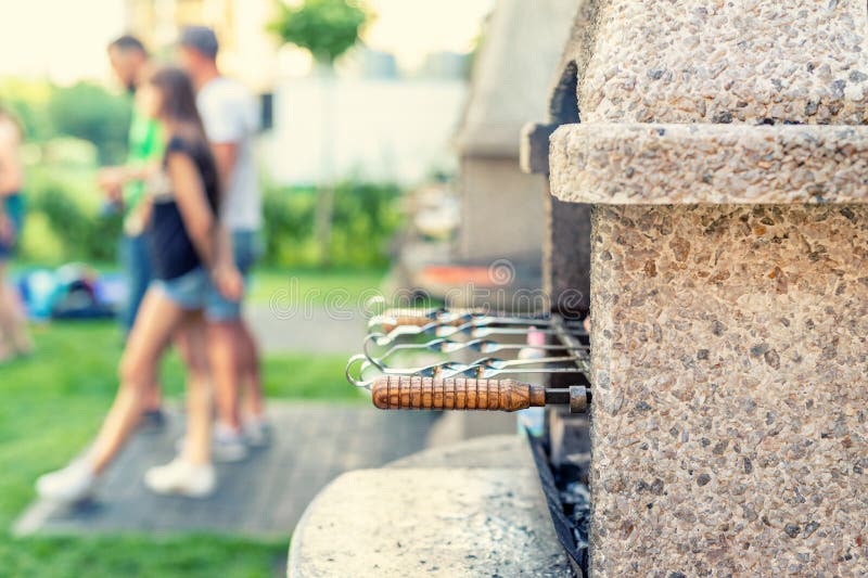 Chimenea de piedra exterior con parrilla y brochetas. CompañÃa de amigos en la barbacoa en el parque o patio trasero con césped foto de archivo libre de regalías Chimenea de piedra exterior con parrilla y brochetas. CompañÃa de amigos en la barbacoa en el parque o patio trasero con césped foto de archivo libre de regalías