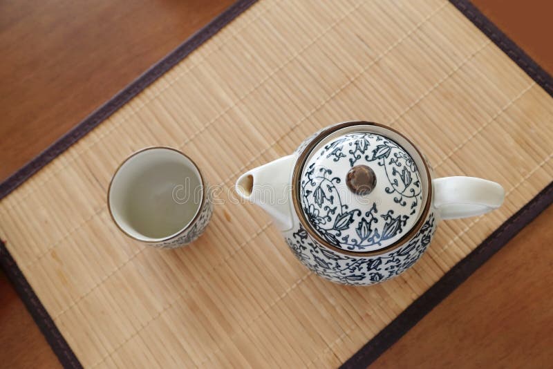 Chinaware blue and white porcelain teapot and empty cup on bamboo tablemat