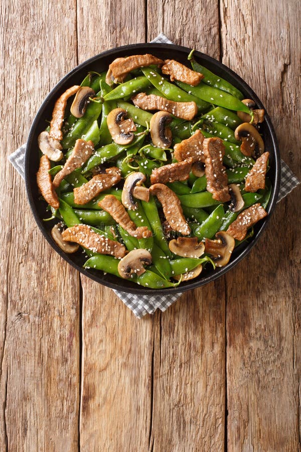 Chinese Roasted beef with mushrooms and pods of green peas, sesame seeds close-up in a plate. vertical top view