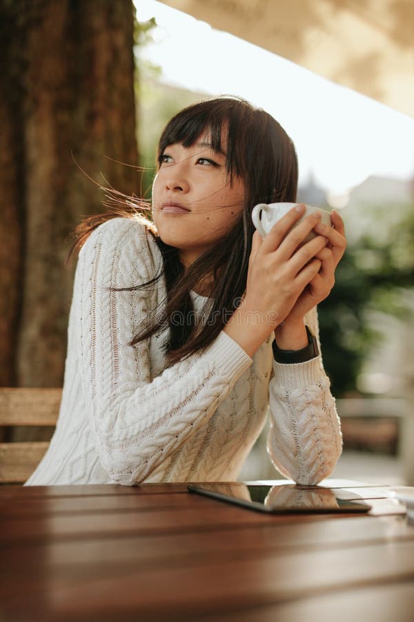 Shot of chinese woman sitting at outdoor cafe holding a cup of coffee and looking away. Shot of chinese woman sitting at outdoor cafe holding a cup of coffee and looking away.