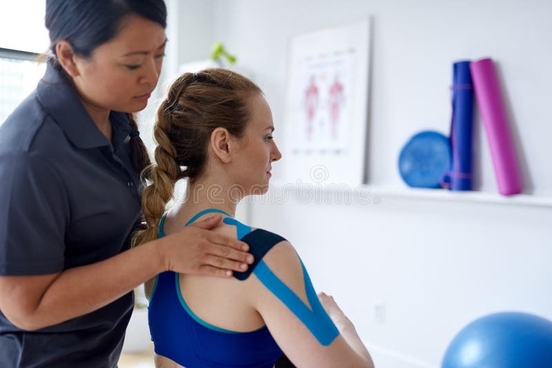 Chinese Woman Massage Therapist Applying Kinesio Tape To The Shoulders