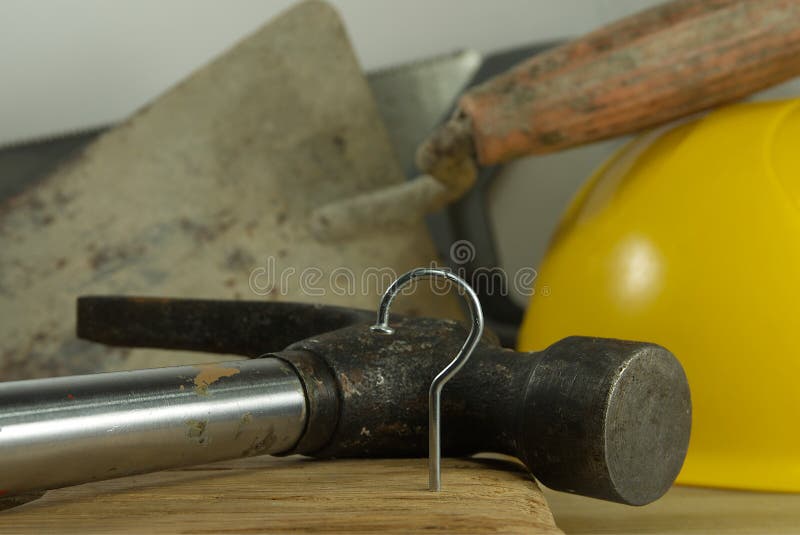 Construction nail shaped as question mark with blurred background of various tools and helmet, construction questions and confusion concept. Construction nail shaped as question mark with blurred background of various tools and helmet, construction questions and confusion concept