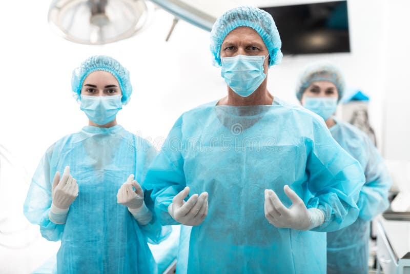 Chirurg und seine Assistenten in den sterilen blauen Kleidern, die im Operationsraum stehen stockbild Chirurg und seine Assistenten in den sterilen blauen Kleidern, die im Operationsraum stehen stockbild