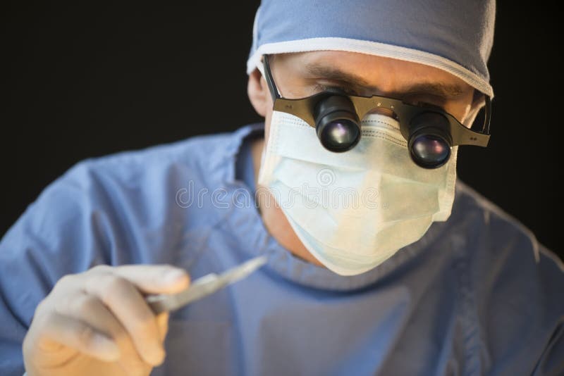 Chirurg-Wearing Mask And-Lupen, die Skalpell halten