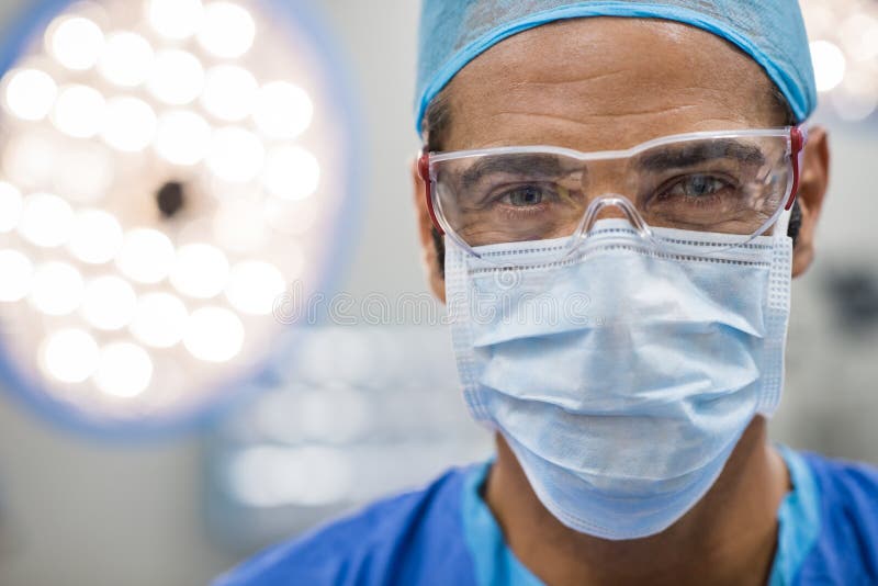 Close up face of surgeon man looking at camera with protective mask. Dental assistant with surgical mask and safety glasses in dental clinic. Happy successful surgeon in a operating room. Close up face of surgeon man looking at camera with protective mask. Dental assistant with surgical mask and safety glasses in dental clinic. Happy successful surgeon in a operating room.
