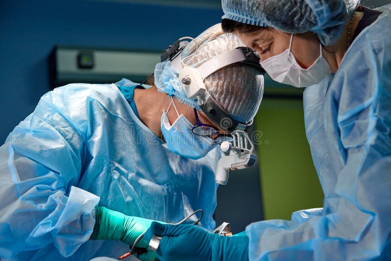 Chirurgo che esegue chirurgia estetica nella sala operatoria dell'ospedale Chirurgo in lenti di ingrandimento d'uso della mascher immagine stock Chirurgo che esegue chirurgia estetica nella sala operatoria dell'ospedale Chirurgo in lenti di ingrandimento d'uso della mascher immagine stock