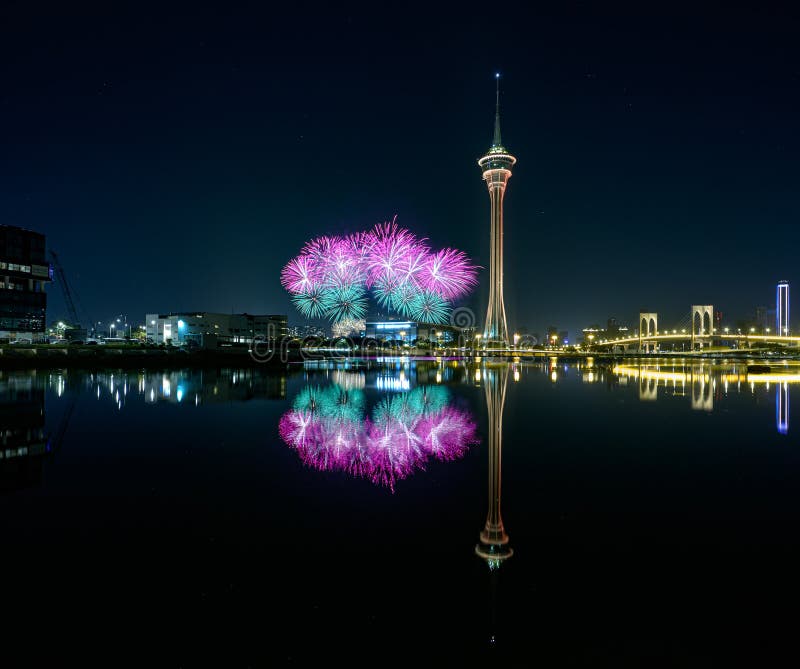 Chispas nocturnas : celebración de torres. Los fuegos artificiales y la torre se reflejan en el agua tranquila que hay debajo