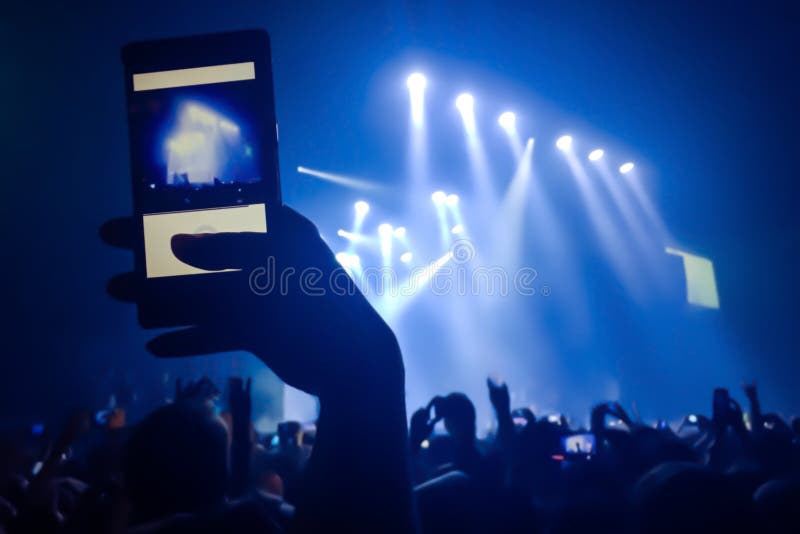 Chiuda su del video della registrazione con lo smartphone durante il concerto Folla al concerto ed alle luci vaghe della fase fotografia stock Chiuda su del video della registrazione con lo smartphone durante il concerto Folla al concerto ed alle luci vaghe della fase fotografia stock