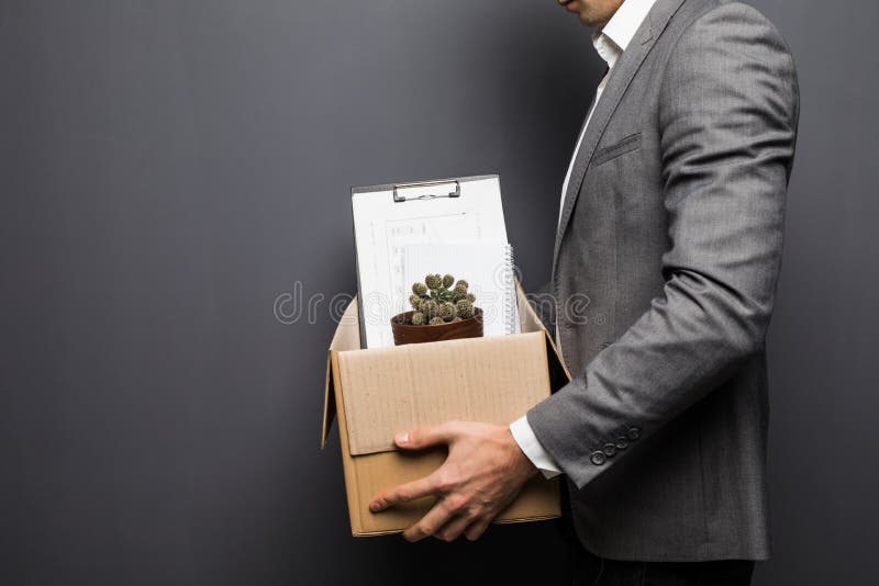 Chiuda su dell'impiegato licenziato dell'uomo che si nasconde dietro la scatola con gli oggetti personali su fondo grigio fotografia stock libera da diritti Chiuda su dell'impiegato licenziato dell'uomo che si nasconde dietro la scatola con gli oggetti personali su fondo grigio fotografia stock libera da diritti